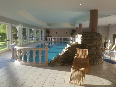 Hell erleuchteter Innenpool mit Balustrade, Steinmauer, blauer Wasseroberfläche und einem Holzliegestuhl.