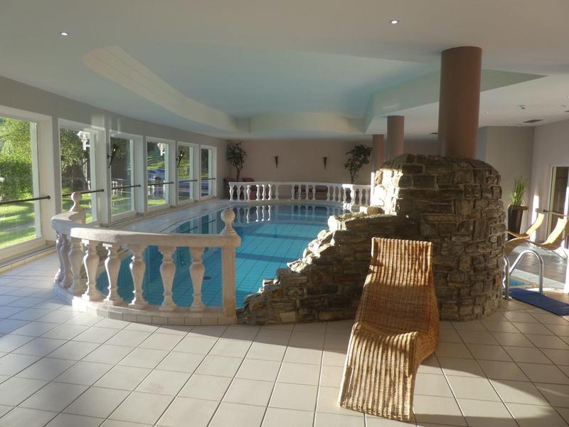 Hell erleuchteter Innenpool mit Balustrade, Steinmauer, blauer Wasseroberfläche und einem Holzliegestuhl.