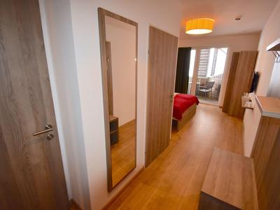 Flur mit Holzfußboden, großem Spiegel und Blick ins Schlafzimmer mit rotem Bett