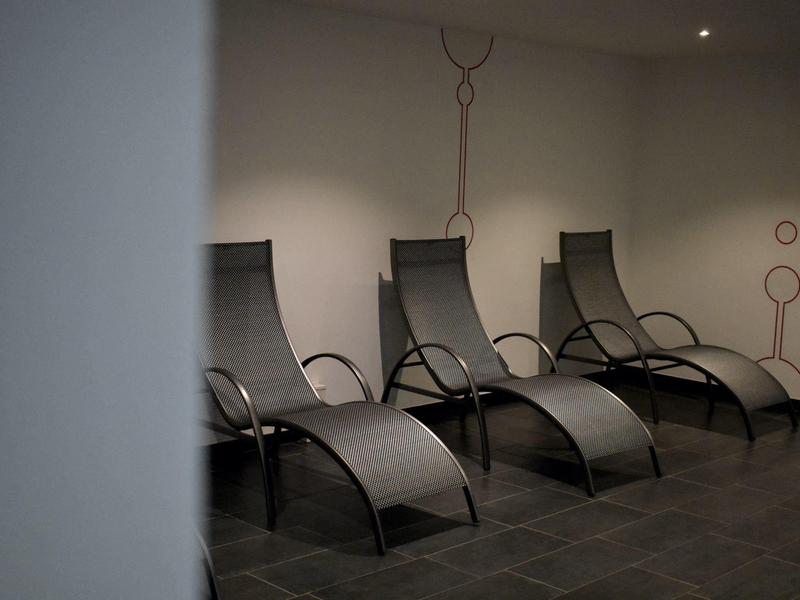 Quatre chaises longues modernes dans un espace intérieur faiblement éclairé aux murs gris.