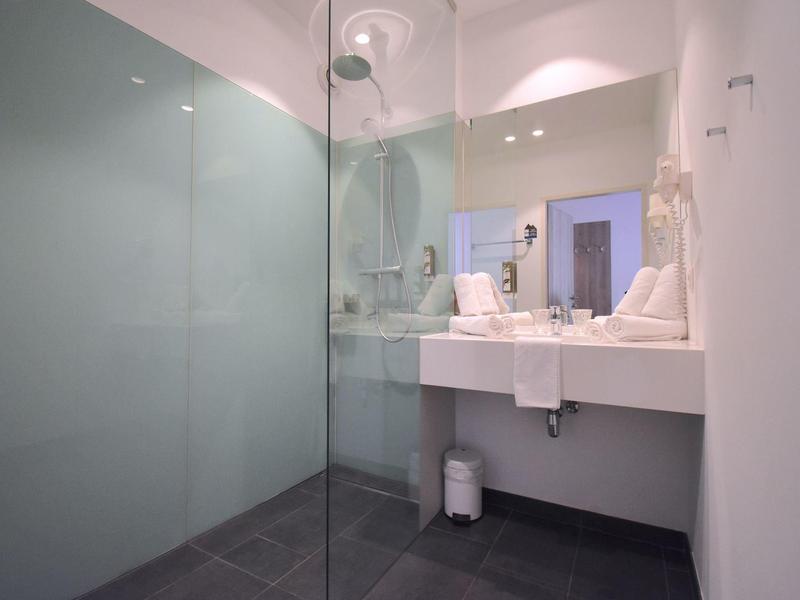 Salle de bains moderne avec douche à l'italienne et lavabo blanc dans une chambre d'hôtel.