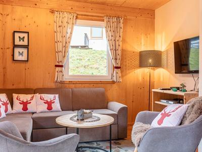 Gezellig zithoekje met grijze bank, rendierkussens en houten wandbekleding in een woonkamer.