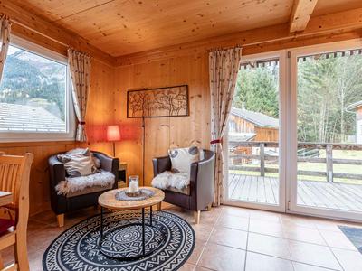 Gezellig woongedeelte in een houten hut met fauteuils, tapijt en uitzicht naar buiten.