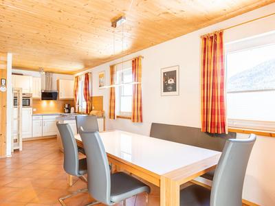 Eetgedeelte met witte tafel, grijze stoelen en geruite gordijnen in een lichte houten hut