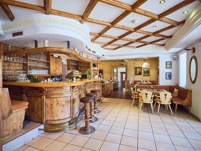 Restaurant lumineux avec bar en bois, tabourets de bar, tables en bois avec chaises et banquette.