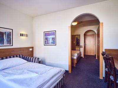 Chambre d'hôtel avec deux lits, moquette bleue, mobilier en bois, arche vers le couloir