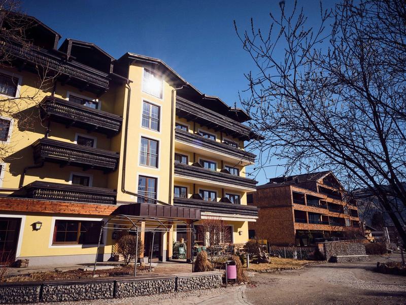 Mehrstöckiges Wohngebäude mit Balkonen bei klarem Himmel und kahlem Baum im Vordergrund.