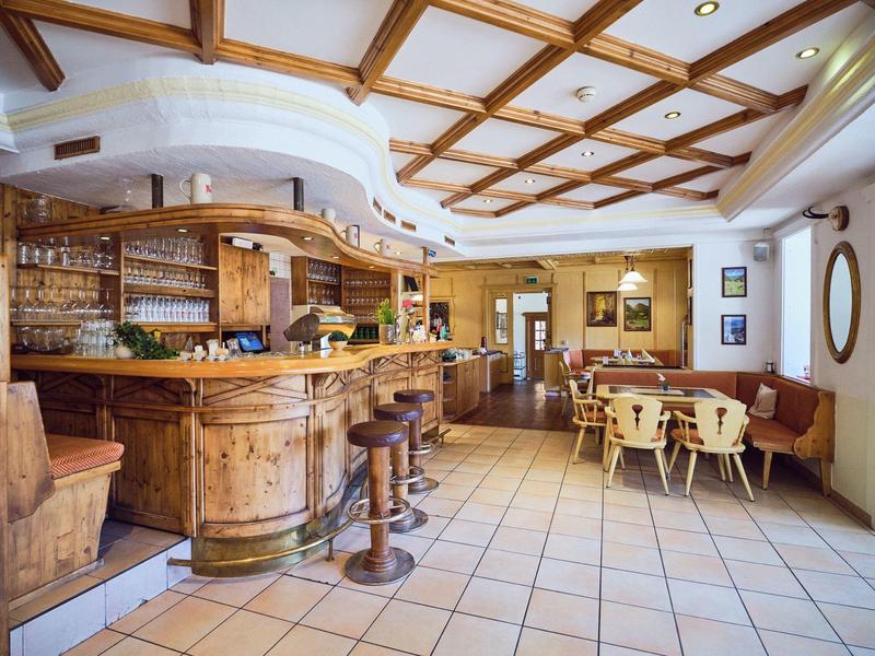 Rustikale Gaststube mit Holzbar, Holzstühlen, Holztischen und hellen Fliesenboden.