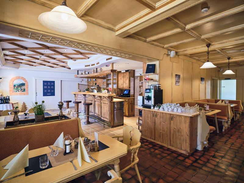 Gemütliches Restaurant mit Holzdecke, Tischen, Stühlen und einer Bar in warmem Licht.