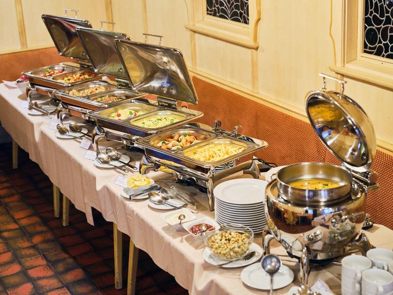 Buffet mit verschiedenen warmen Speisen in Edelstahlbehältern auf einem gedeckten Tisch.