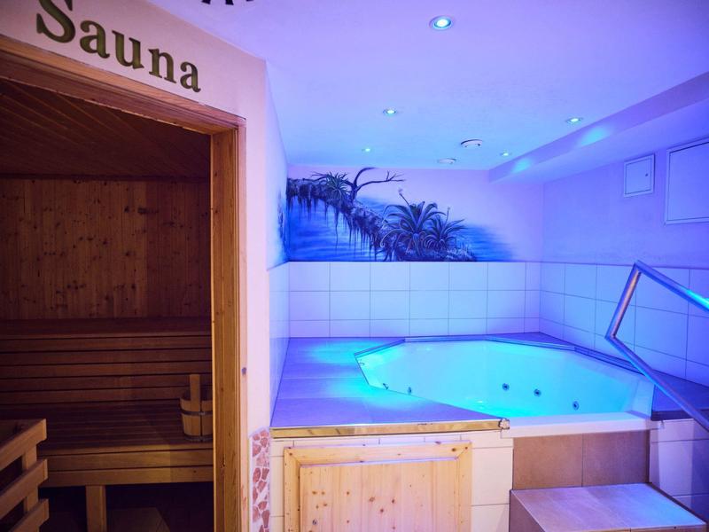 Moderner Wellnessbereich mit Sauna und beleuchtetem Whirlpool, weiße Wände und indirekte blaue Beleuchtung.