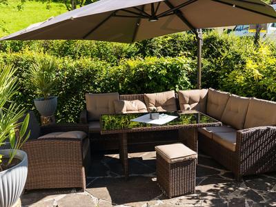 Moderner Außenbereich mit braunen Rattanmöbeln, Sonnenschirm und grüner Bepflanzung.