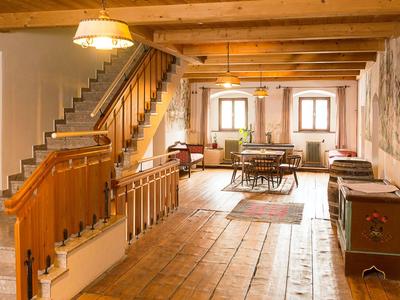 Ein rustikaler Innenraum mit Holztreppe, Holzbalken und gemütlichem Essbereich unter natürlichem Licht.