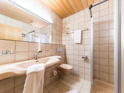 Hell beleuchtetes Badezimmer mit Waschbecken, Spiegel, Dusche und Toilettenpapierhalterung.