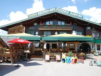 Gemütliches Hotel mit Restaurant und Außenbereich unter blauem Himmel in Alpenarchitektur.