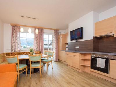 Helles Wohnzimmer mit Esstisch, Stühlen, Sofa und moderner Küchenzeile mit Elektrogeräten.