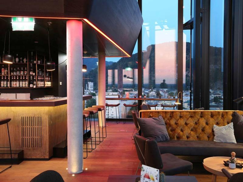 Nowoczesna część hotelowego baru z sofą, stolikami i dużymi oknami z widokiem na góry.