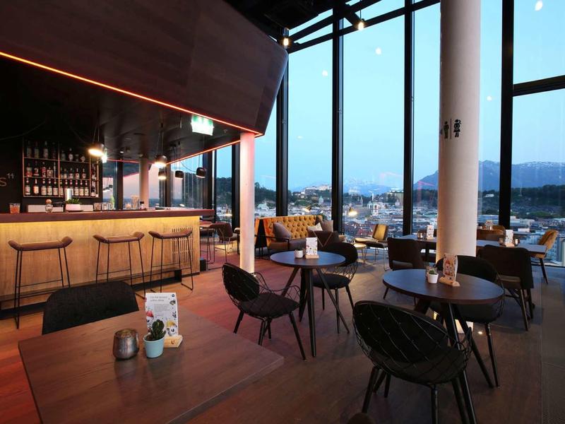 Nowoczesna restauracja z drewnianym wystrojem, wygodnymi krzesłami i dużymi szklanymi oknami z widokiem na miasto.