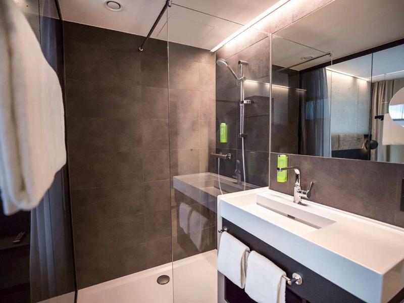 Nowoczesny prysznic hotelowy ze szklaną przegrodą, białymi ręcznikami i stylową umywalką.