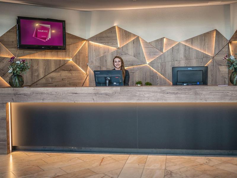 Réception d'hôtel moderne avec boiseries, deux écrans et personnel à l'accueil.