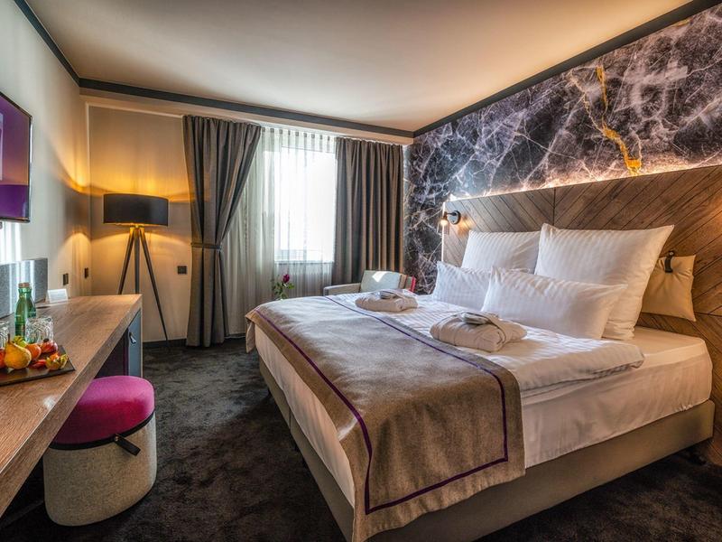 Chambre d'hôtel moderne avec grand lit, décoration murale et fenêtre avec rideaux gris.