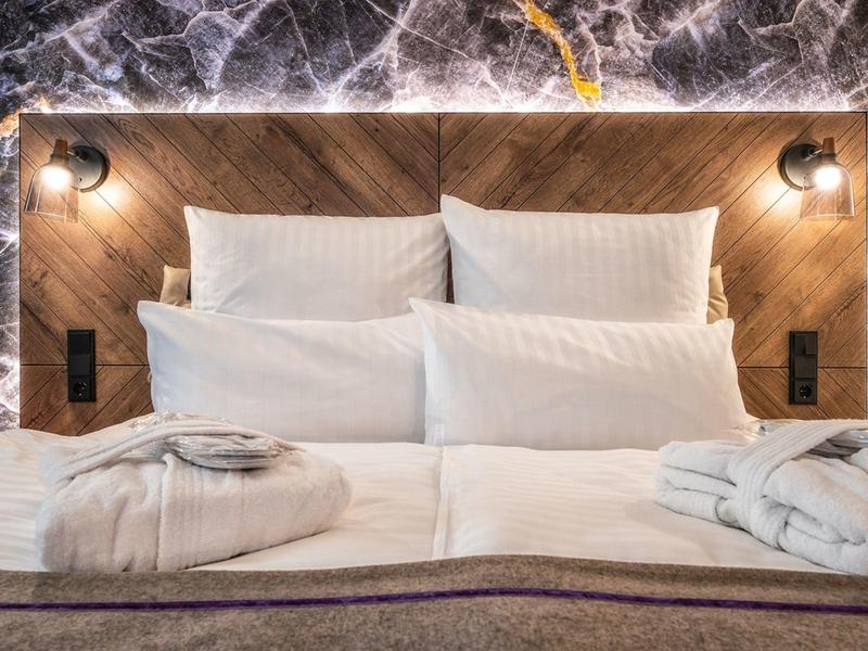 Lit d'hôtel confortable avec linge blanc, peignoirs et une tête de lit moderne en marbre.