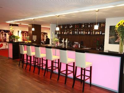 Moderner Barbereich mit rosa beleuchtetem Tresen, sieben weißen Barhockern und Sonnenblumen-Dekor.