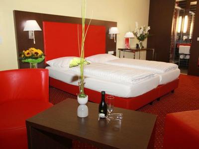 Hotelzimmer mit zwei Einzelbetten, rotem Dekor und einem Tisch mit einer Weinflasche und Gläsern.