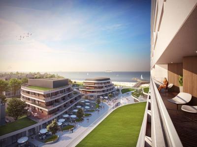 Moderne Gebäude mit Balkonen, grüner Rasenfläche und Blick aufs Meer unter klarem Himmel.