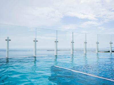 Infinity-Pool mit klarem blauem Wasser und Glasgeländer vor einem hellen Himmel am Meer.