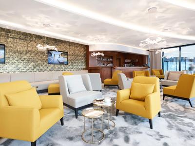 Modern eingerichteter Aufenthaltsraum mit gelben Sesseln, grauen Sofas und großen Fenstern.