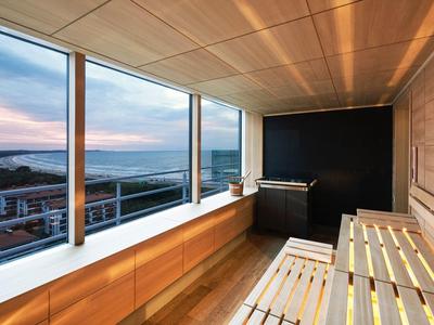 Moderner Saunaraum mit großen Fenstern, Holzverkleidung, Holzbank und Saunaofen, beruhigender Abendhimmel.