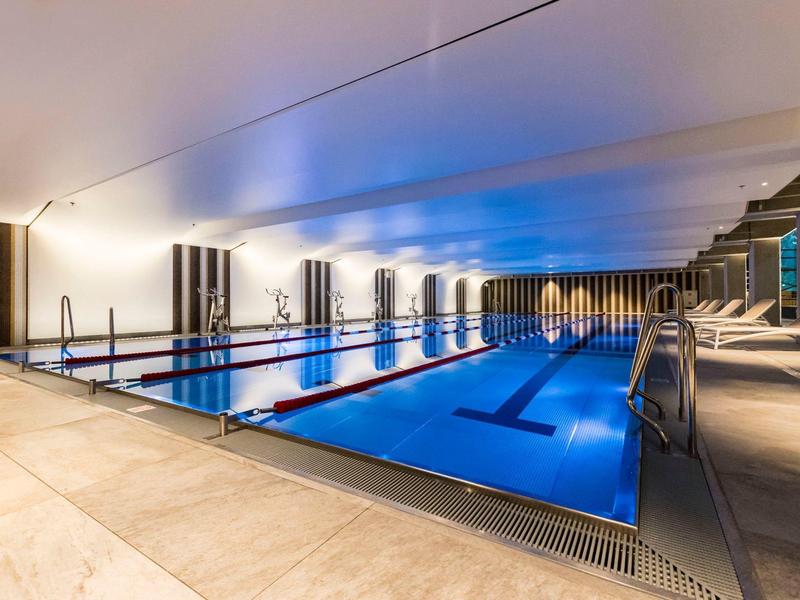 Moderner Innenpool mit blauer Beleuchtung, Liegestühlen und heller Marmorfliesen-Umrandung.