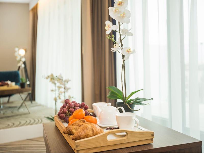 Holztablett mit Tee, Gebäck, Orangen und Trauben auf Tisch vor Fenster mit weißen Vorhängen.