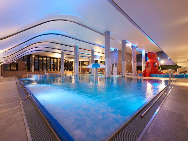 Moderner Indoor-Pool mit blauer Beleuchtung und stilvollem Wellen-Dach.