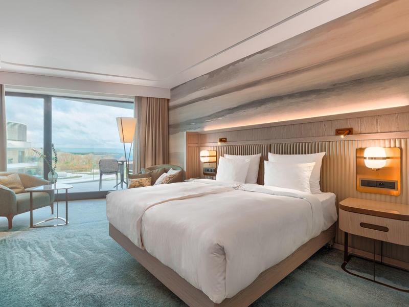 Modernes Hotelzimmer mit zwei Betten, Sitzbereich und Panoramafenstern mit Bergblick.