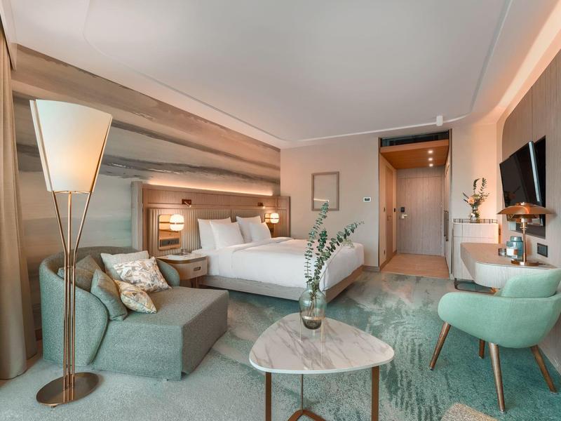 Modern eingerichtetes Hotelzimmer mit Doppelbett, Sofa und sitzbereich mit grünem und beigem Farbton.