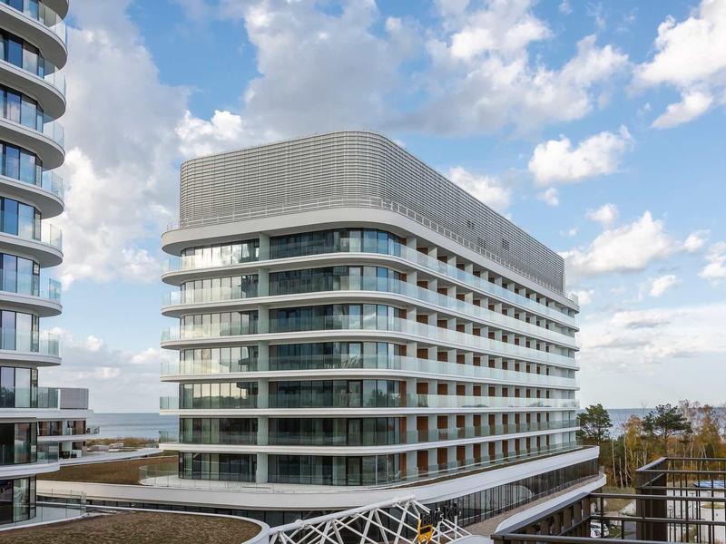 Modernes Bürogebäude mit abgerundeten Ecken und hellen Glasfassaden unter blauem Himmel.