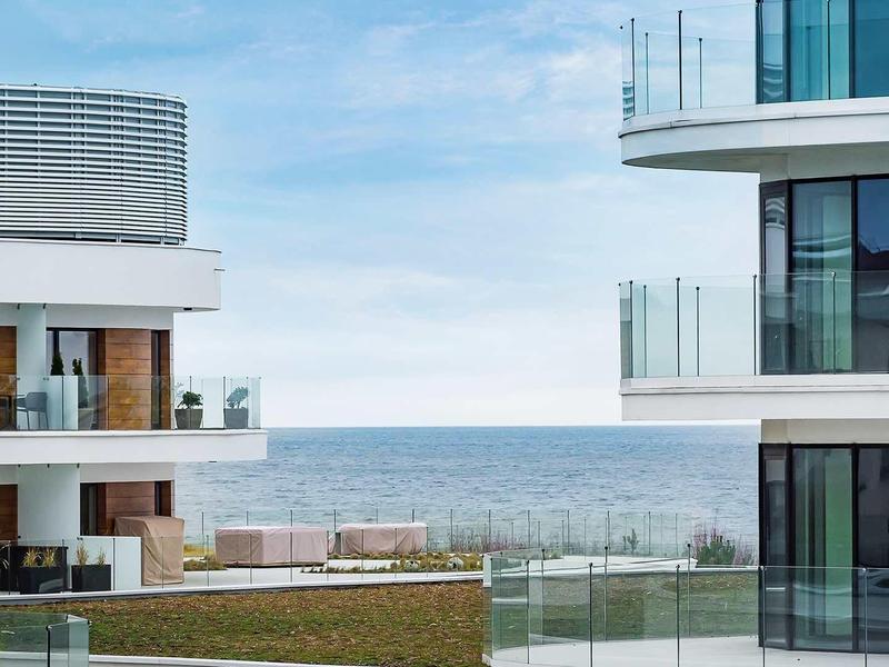 Meerblick zwischen modernen Wohngebäuden mit Glasbalkonen und grünen Dachterrassen.