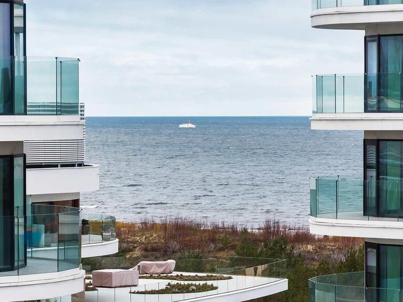 Moderne Glasbalkone an weißen Wohngebäuden mit Meerblick und bewölktem Himmel im Hintergrund.