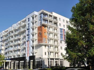 Moderner weißer Mehrfamilienwohnblock mit Balkonen und klarer Linienführung bei blauem Himmel.