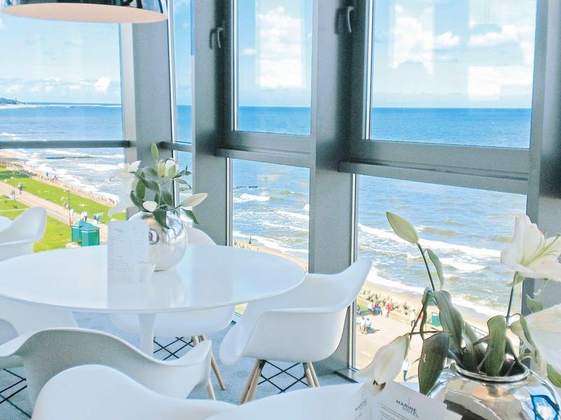 Heller Essbereich mit weißen Stühlen und runder Tisch vor großen Fenstern mit Meerblick.