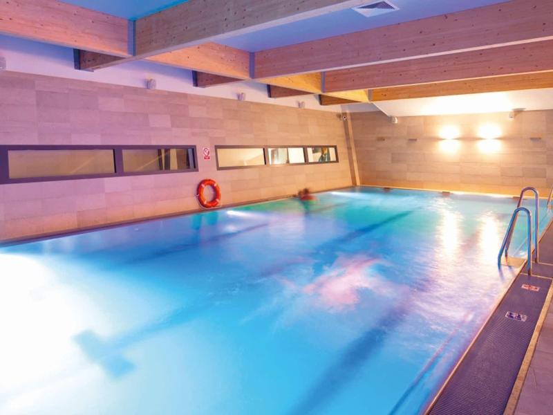 Innen-Schwimmbad mit blauem Wasser, Holzverkleidungen und Deckenbalken aus Holz.