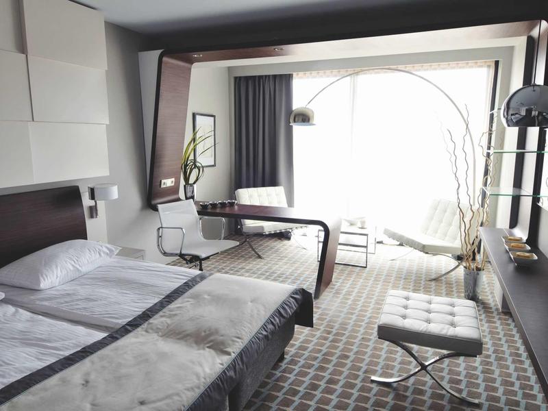 Modernes Hotelzimmer mit Doppelbett, großem Fenster, Schreibtisch und minimalistischer Einrichtung.