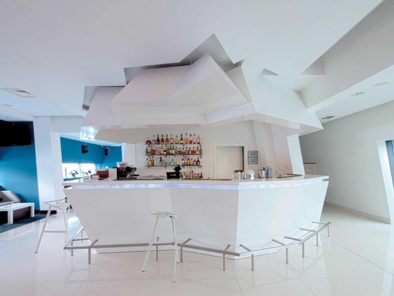 Moderner weißer Bartresen mit transparenten Hockern in hellem, minimalistischem Raum.