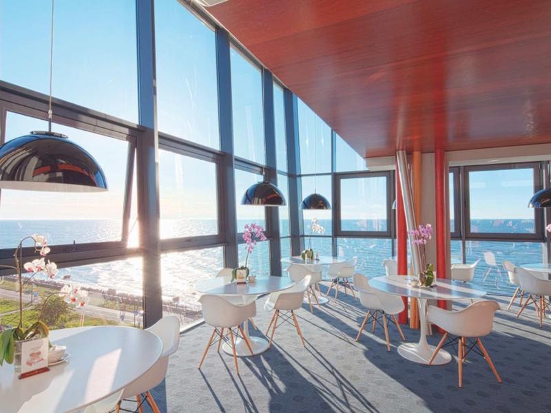 Modernes Café mit weißen Stühlen, großen Fenstern und Blick auf das Meer bei Sonnenuntergang.