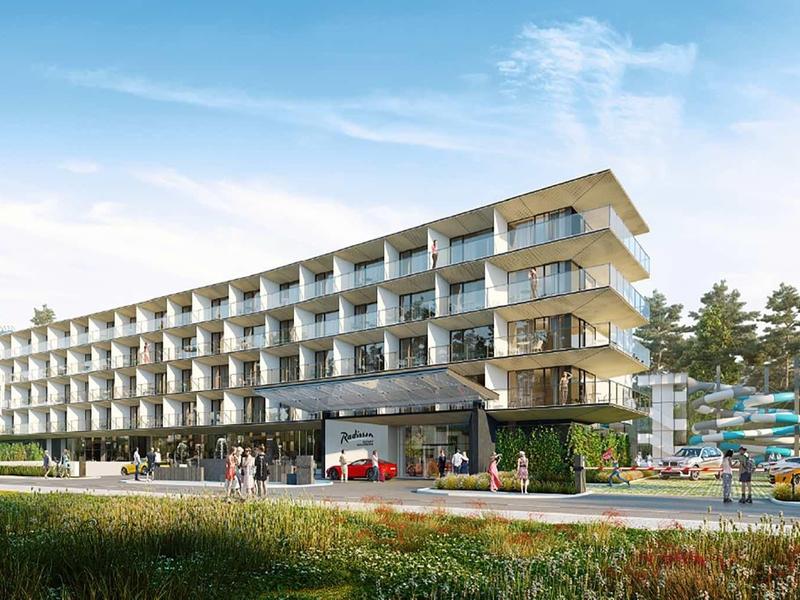 Modernes, langgestrecktes Hotelgebäude mit Balkonen, umgeben von Bäumen und blauem Himmel.