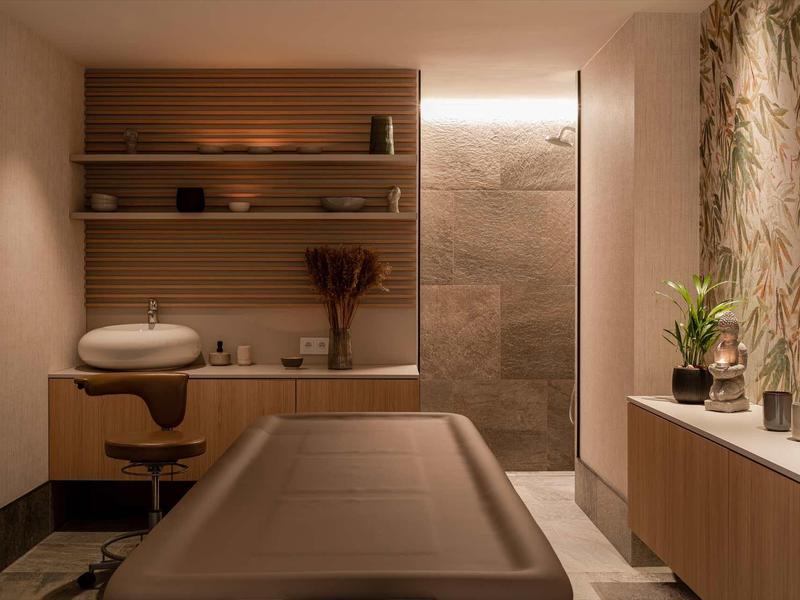 Modernes, warm beleuchtetes Behandlungszimmer mit Holzregalen, gemütlichem Stuhl und Pflanzen.