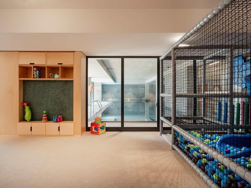 Kinder-Spielzimmer mit Holzregal, Bällebad und Rutschbahn hinter schwarzem Netz. Helles, offenes Design.