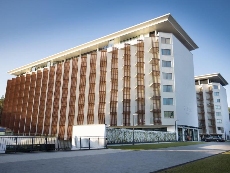 Modernes, mehrstöckiges Gebäude mit brauner Holzverkleidung und weißem Putz vor blauem Himmel.